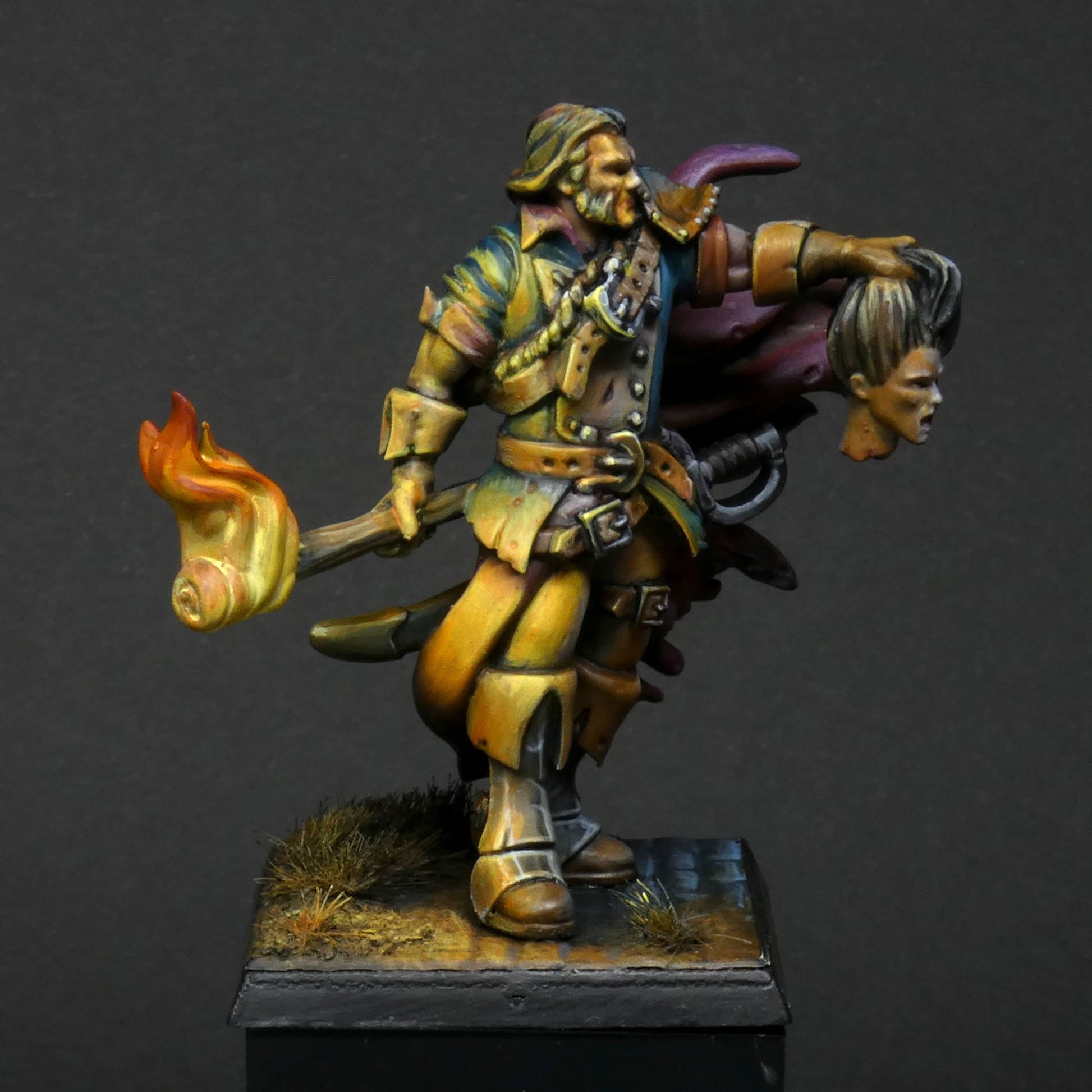 a side view of 32mm scale miniature of Cristof Witchbane, a rugged witch hunter wielding a flaming torch and a severed witch's head.  The model is viewed painted beautifully with excellent lighting effects from the fire of the torch. 