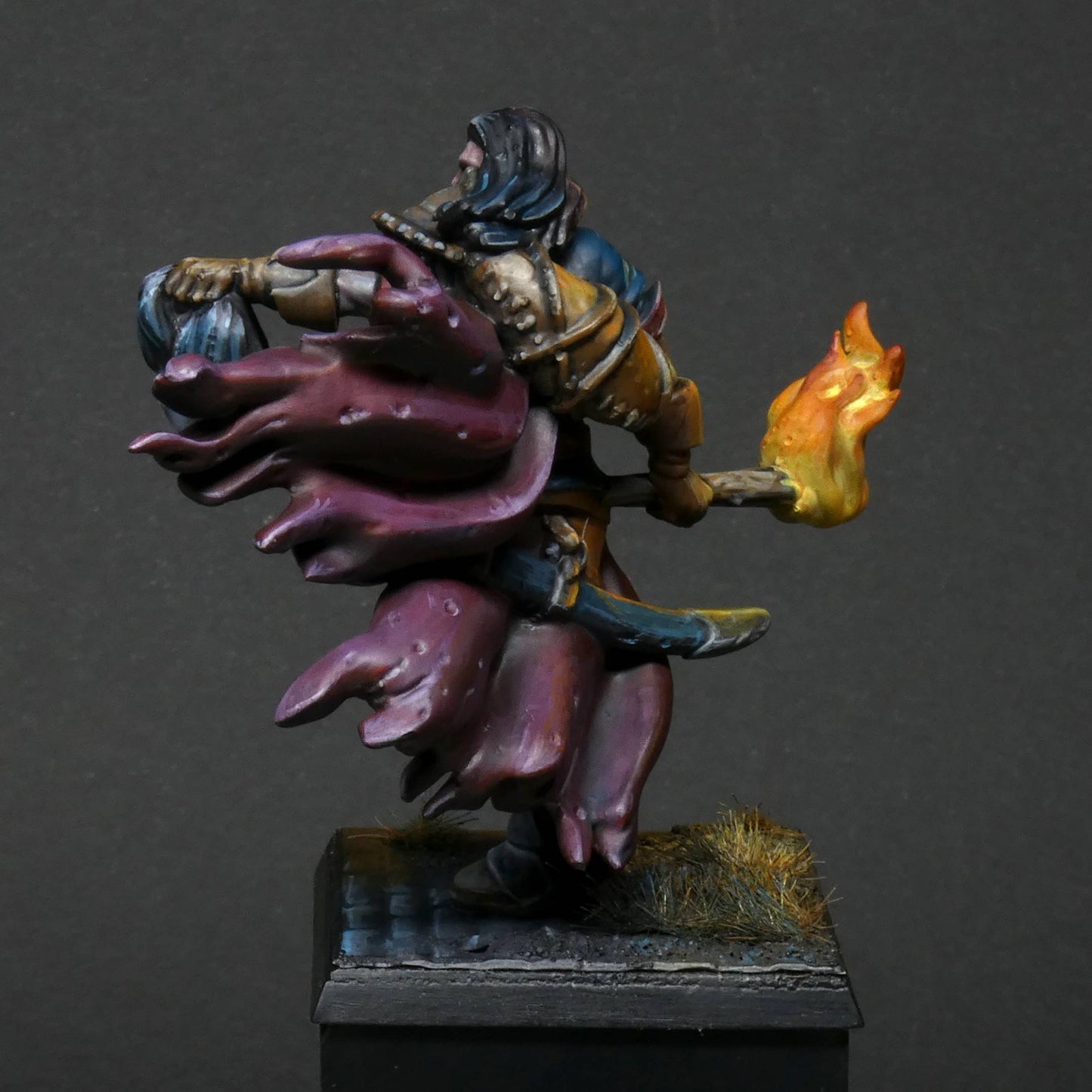 a rear/ back view 32mm scale miniature of Cristof Witchbane, a rugged witch hunter wielding a flaming torch and a severed witch's head.  The model is viewed painted beautifully with excellent lighting effects from the fire of the torch. 