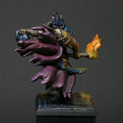 a rear/ back view 32mm scale miniature of Cristof Witchbane, a rugged witch hunter wielding a flaming torch and a severed witch's head.  The model is viewed painted beautifully with excellent lighting effects from the fire of the torch. 