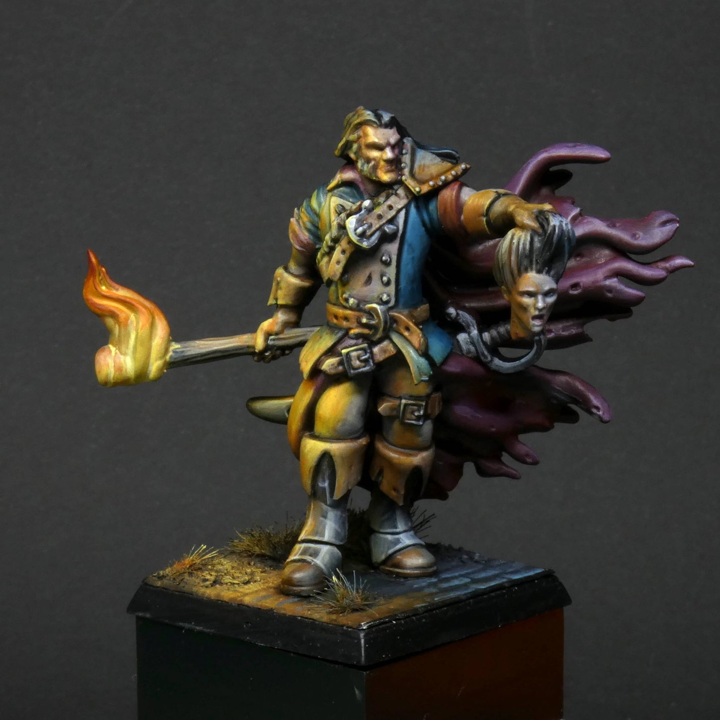 a 32mm scale miniature of Cristof Witchbane, a rugged witch hunter wielding a flaming torch and a severed witch's head.  The model is viewed painted beautifully with excellent lighting effects from the fire of the torch. 