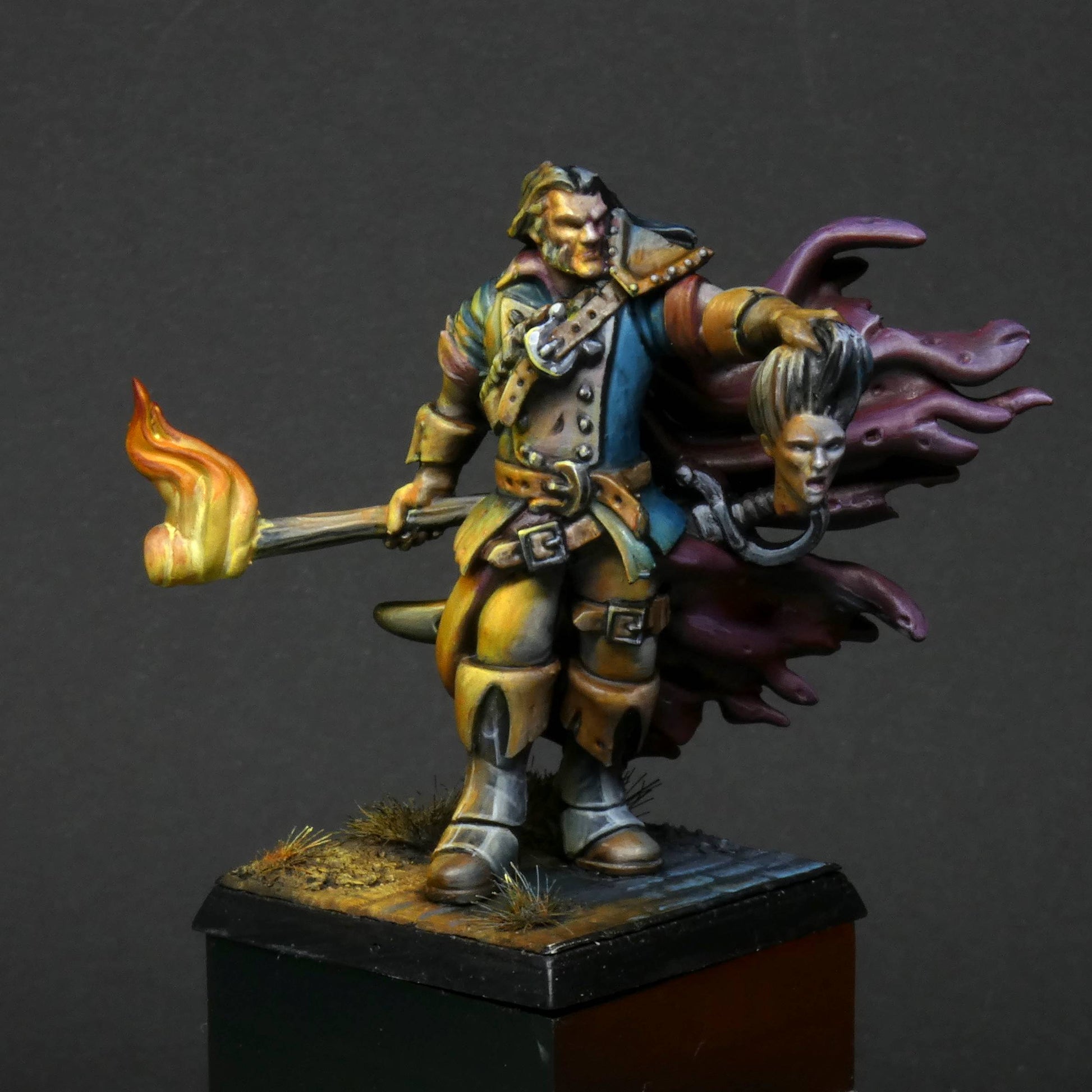 a 32mm scale miniature of Cristof Witchbane, a rugged witch hunter wielding a flaming torch and a severed witch's head.  The model is viewed painted beautifully with excellent lighting effects from the fire of the torch. 